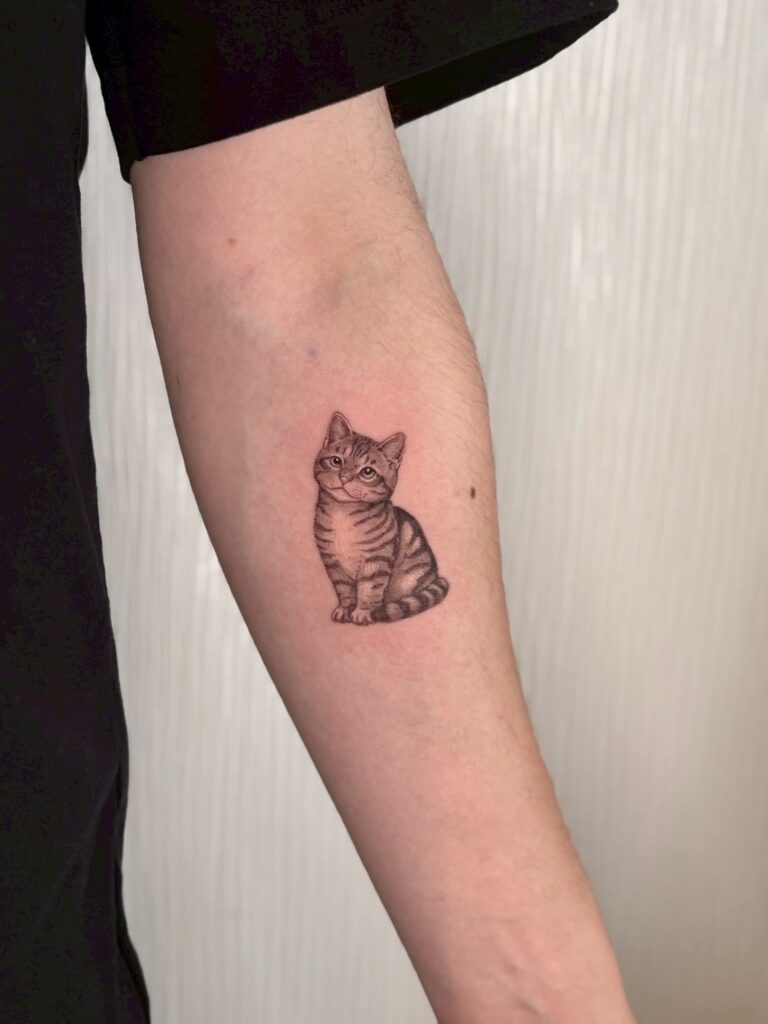 腕に子猫の顔と姿を黒の濃淡で描いたタトゥー