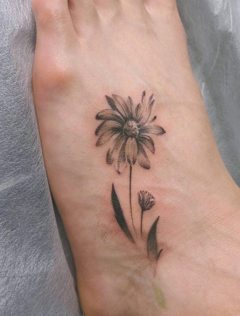 脚に一輪の花と小さな蕾を描いた、細い線と陰影のタトゥー